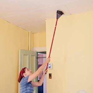 Young woman sweeping the ceiling with a broom to get rid of dust.