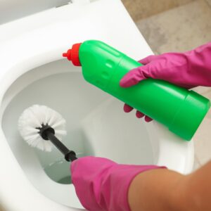 Woman in rubber pink gloves cleans toilet bowl with brush